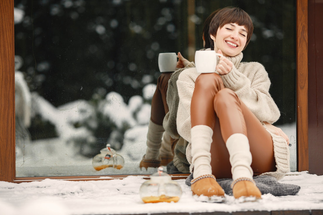 Nie mehr kalte Füße im Bett - Frau sitzt lächelnd mit warmen Füßen in Hausschuhen 