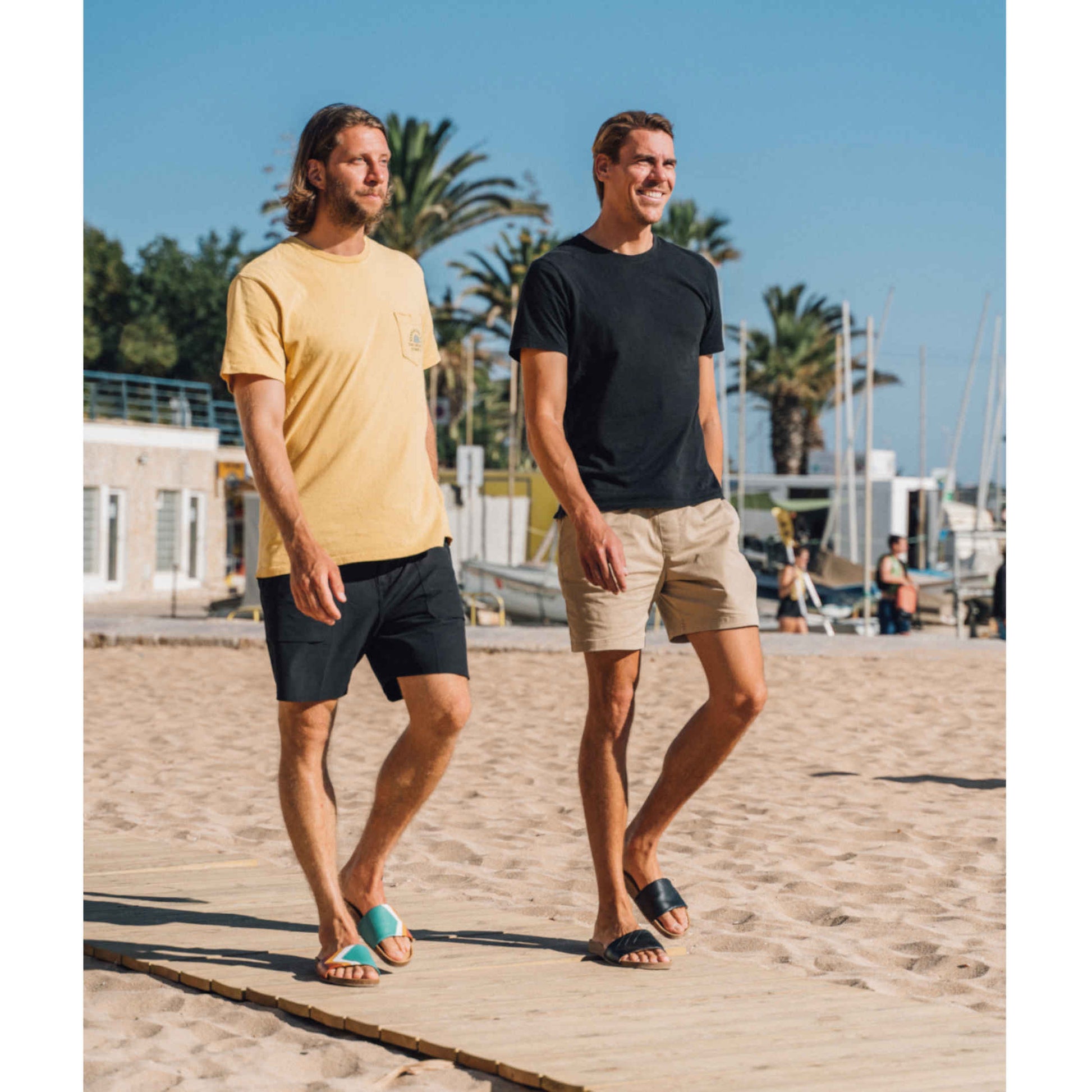 Vegane schwarze Sandalen, Marke Fünve, Modell: YIN, zwei Surferboys in Sandalen am Strand, Marke Fünve