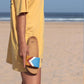 Blaue Sandalen, vegan mit Fußbett, Farben Azur, Weiß, Terracotta, Senf; Marke Fünve, Modell Sky, Einzelne Sandale in der Hand am Strand